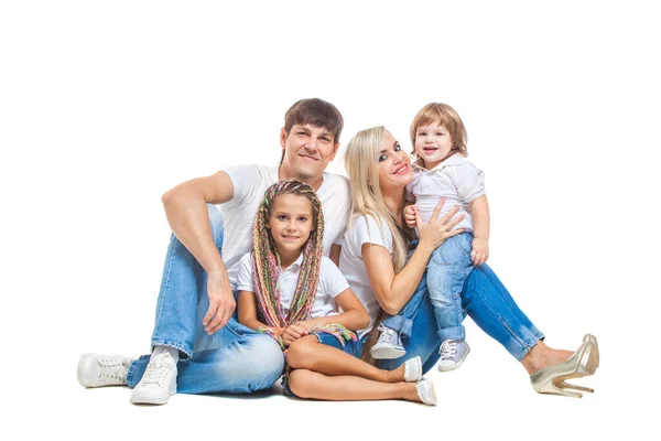 Padres felices con un hijo y una hija en camisetas blancas y vaqueros azules se divierten juntos posando sentados en el suelo aislados sobre fondo blanco — Foto de Stock