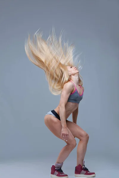 Σέξι αθλητική ξανθιά κοπέλα πέταξε τα μακριά μαλλιά της απομονωμένα σε γκρι φόντο — Φωτογραφία Αρχείου