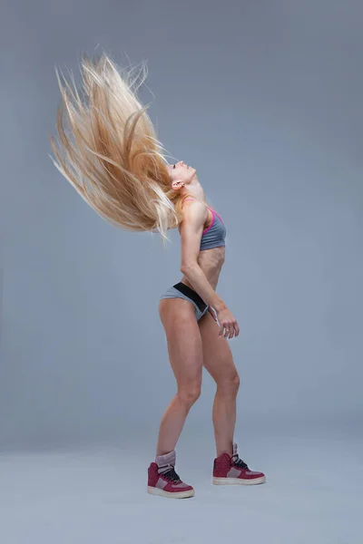 Sexy atletisch blond meisje gooide haar lange haar geïsoleerd op grijze achtergrond — Stockfoto