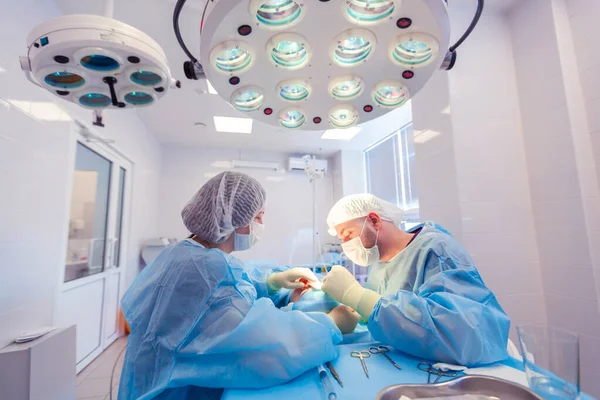 A férfi sebész sebészeti beavatkozásokat végez a műtőben, míg asszisztense a beteg állapotát figyeli. — Stock Fotó