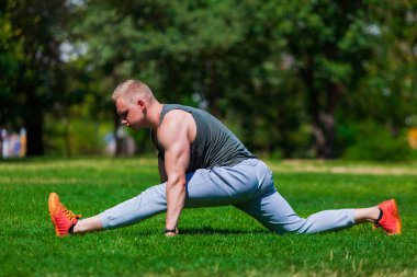 Genç kaslı adam yoga yapıyor ve açık havada bir yaz parkında esniyor.