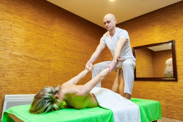 Vinkel vy skott på massör drar kvinna armar gör traditionell thailändsk massage på kvinnlig kropp i spa salongen. Begreppet skönhetsbehandling — Stockfoto