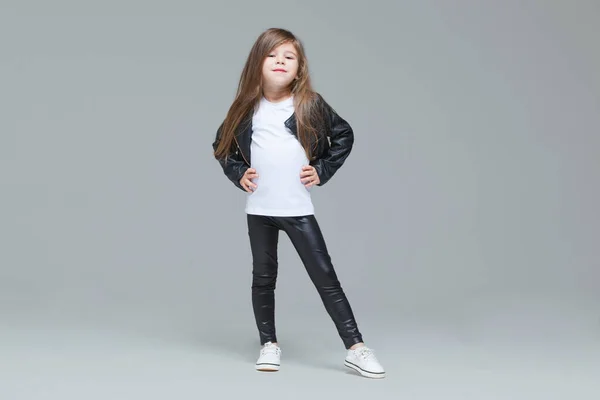 Bebe Fille Aux Cheveux Longs En Veste Et Leggings En Cuir Noir Se Tient Debout En Studio Sur Fond Gris Conserve Longue Stock Photo