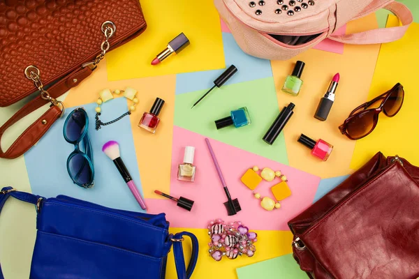 Things from open lady purses. Cosmetics and women's accessories fell out of different handbags on colourful background. Top view.