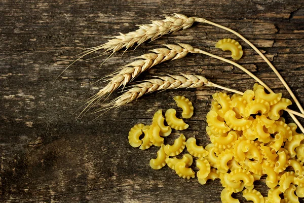 Pasta and wheat ears on wooden background.