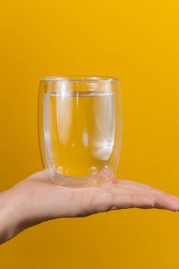 Sarı arka planda bir elde cam. Sağlıklı beslenme. Yakın çekim.