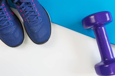 Beyaz arka planda spor aletleri, spor ayakkabıları, paspas ve dambıl. Karşıt aksesuarlar