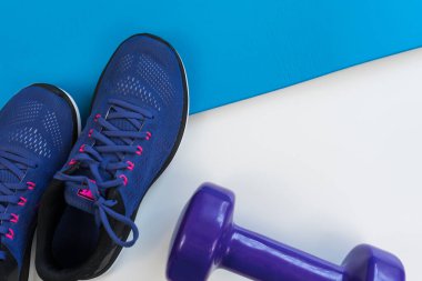 Beyaz arka planda spor aletleri, spor ayakkabıları, paspas ve dambıl. Karşıt aksesuarlar