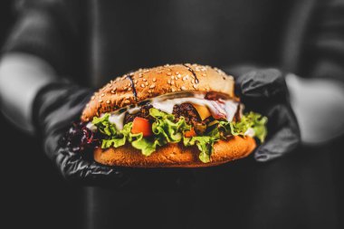 Siyah beyaz bir fotoğrafta renkli burger. Kötü yemek, fast-food. Hamburger ellerinde.