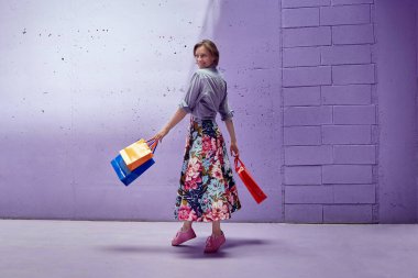 Elinde paketler olan genç ve güzel bir kız. Uzun açık etekli ve açık pembe bluzlu bir kız mağazadan çıkıyor..