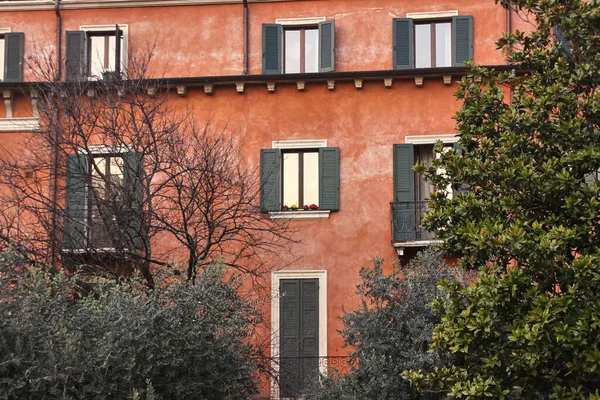Muur van een huis met rood oud stucwerk en grijze raamluiken — Stockfoto