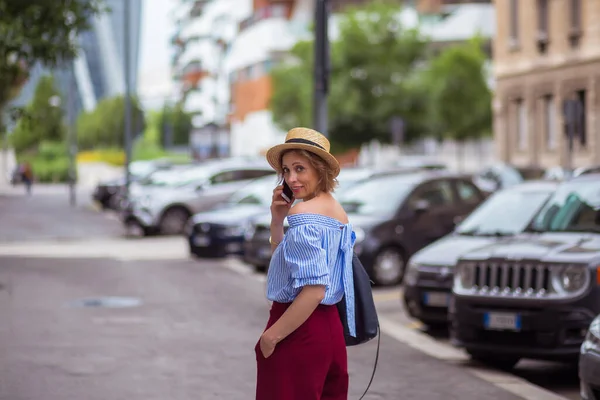 A menina de chapéu caminha pela cidade e fala ao telefone — Fotografia de Stock