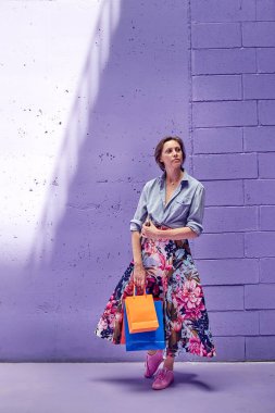 Elinde paketler olan genç ve güzel bir kız. Uzun açık etekli ve açık pembe bluzlu bir kız mağazadan çıkıyor..