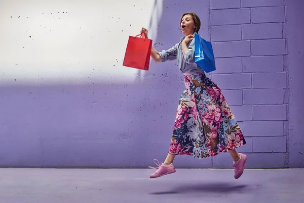Joven hermosa chica corre con bolsas de compras en sus manos. Una chica con una falda larga y brillante y un top rosa pálido está caminando desde la tienda . — Foto de Stock