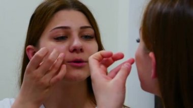 Kadın aloe vera yaprağı kullanıyor ve aynaya bakıyor.