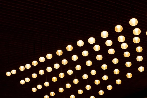 Small round pendant lights on the ceiling with vertical stripes. Wooden canvas. Golden lighted lamps.