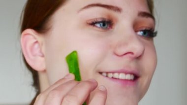 Gülümseyen kadın beyaz arka planda aloe vera yaprağıyla poz veriyor.