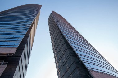 Mavi gökyüzüne karşı megalopolis yakınlarında duran iki mavi ve gri gökdelen. Milan 01.20.