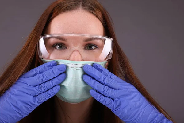 Portrait of a nurse wearing a medical mask, gloves and glasses on grey background