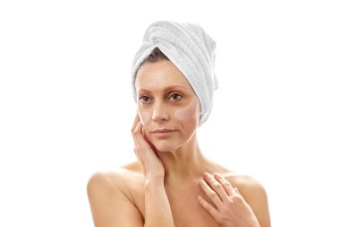 Kafasında beyaz bir havlu olan güzel bir kadın göz bantlarıyla yüz yenileme ameliyatı yapıyor. Beyaz izole arkaplan.