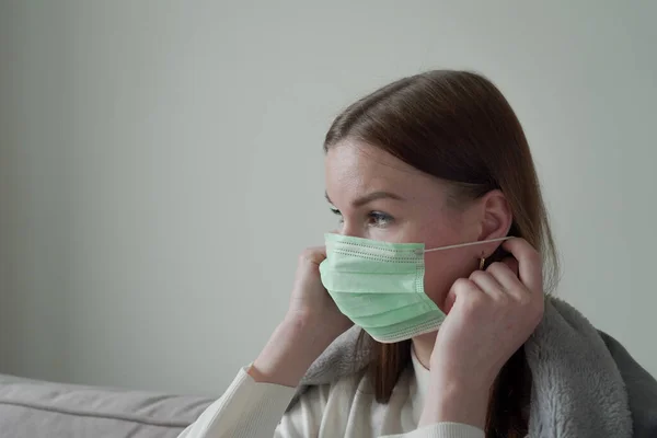 Hermosa joven se pone una máscara médica verde en la cara. Vista lateral. Orvi, coronovirus, gripe, infecciones respiratorias agudas . —  Fotos de Stock