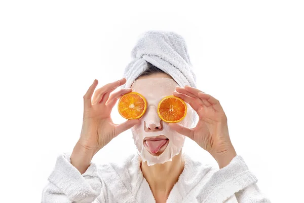 En rolig kvinna pekar ut sin tunga och håller apelsinskivor nära ögonen. Tygmask. Isolerad på en vit bakgrund. — Stockfoto