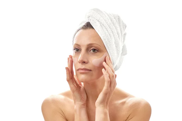 Uma mulher bonita com uma toalha branca na cabeça faz um rejuvenescimento facial com manchas nos olhos. Branco fundo isolado . — Fotografia de Stock