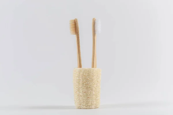 Two toothbrushes made of natural wood are turned away from each other inserted into a natural ecological loofah. on white background. — Stock Photo, Image