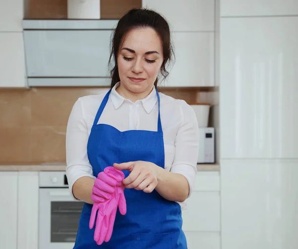 A fiatal, gyönyörű lány rózsaszín kesztyűt vesz fel a takarításhoz. A lány takarít. Professzionális tisztítás — Stock Fotó
