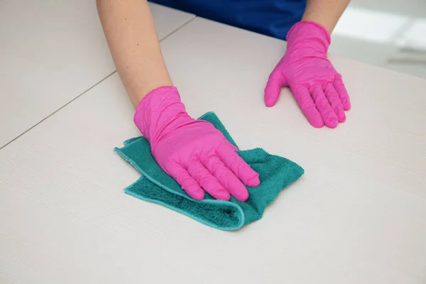 Een hand in een roze handschoen veegt een wit oppervlak af met een blauwe doek om schoon te maken. — Stockfoto