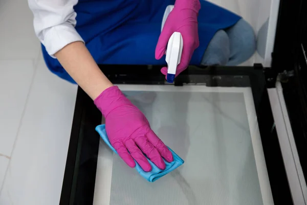 Een meisje in roze rubberen handschoenen wast een oven met een doek en wasmiddel met een spray. — Stockfoto