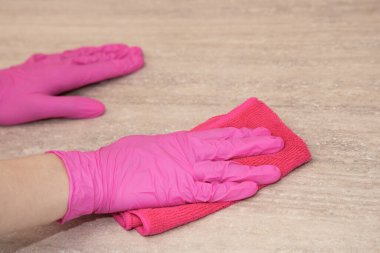 Pembe lastik eldivenli bir kız mikrofiber bezle ahşap bir yüzeyi yıkıyor..