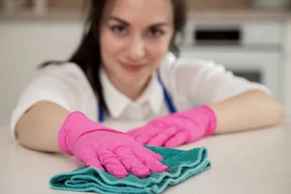 Close-up van een brunette die de keuken schoonmaakt en glimlachend naar de camera kijkt. Het meisje is buiten beeld. Het belangrijkste ding in het frame zijn handschoenen voor het reinigen. — Stockfoto