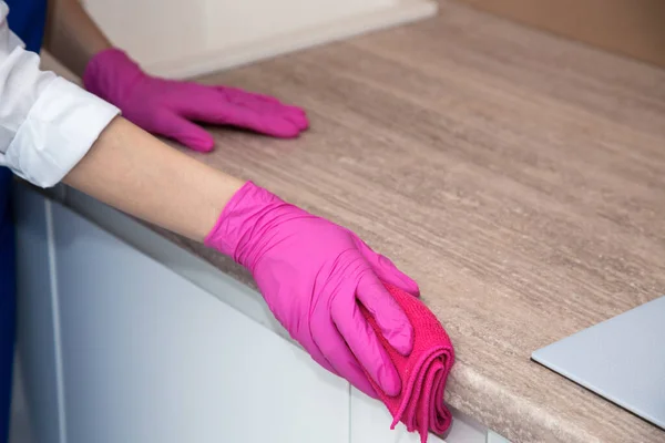 Een meisje in roze rubberen handschoenen wast een kastoppervlak met een microvezel doek — Stockfoto