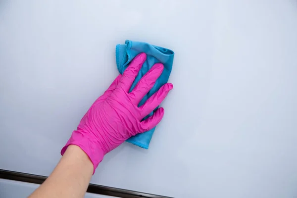 Een hand in een roze handschoen veegt een wit glanzend oppervlak af met een blauwe microvezeldoek. Huisreiniging. — Stockfoto