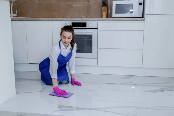 Bella ragazza lava il pavimento con le mani in guanti rosa. Sullo sfondo di una bella cucina bianca moderna . — Foto Stock