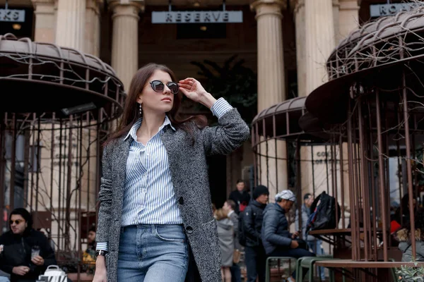 Uma jovem com um casaco cinza, camisa azul e óculos deixa o café . — Fotografia de Stock