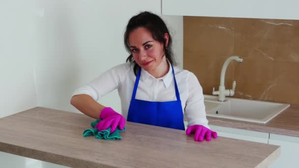 Een brunette maakt schoon en lacht naar de camera. Wrijft een tafel van licht hout. Roze handschoenen voor reiniging. — Stockvideo