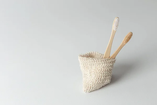 Dos cepillos de dientes de madera natural se encuentran uno al lado del otro en una bolsa ambiental. cero residuos. sobre un fondo gris . — Foto de Stock