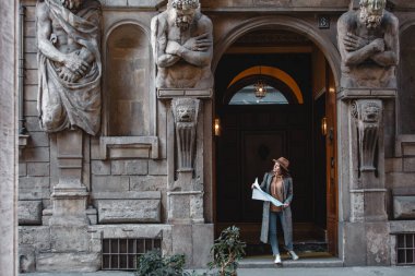 Genç, güzel bir turist kız elinde bir haritayla güzel bir binanın kemerinde duruyor..
