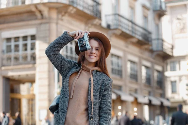 Een jong meisje met een elegante bruine hoed houdt de camera verticaal en maakt foto 's. — Stockfoto