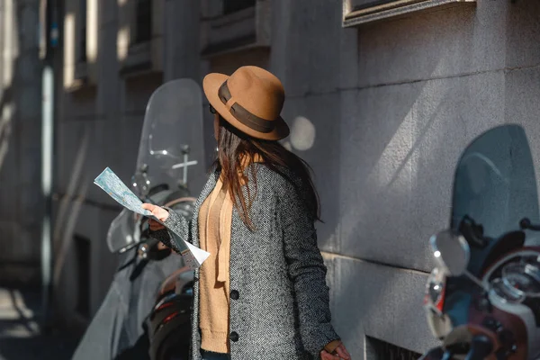 Красивая девушка турист в очках и коричневая модная шляпа с картой в руке ищет, куда пойти. Рядом мотоциклы, скутеры. . — стоковое фото