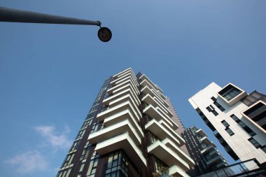 Ön planda bir sokak lambası ve arka planda mavi gökyüzüne karşı bir apartmanın koyu kahverengi fütüristik mimarisi var. 01.2020 Milano