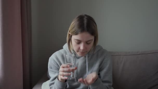 Een ziek meisje, moe van medicijnen, neemt een pil en drinkt het met water met een doorzichtig glas. — Stockvideo