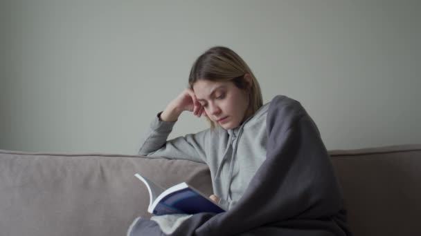 Das blonde Mädchen mit Kurzhaarschnitt sitzt krank zu Hause in Quarantäne und liest ein Buch. — Stockvideo