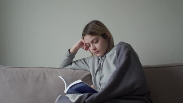 La blonde avec une coupe de cheveux courte est malade assise à la maison en quarantaine et lit un livre . — Video