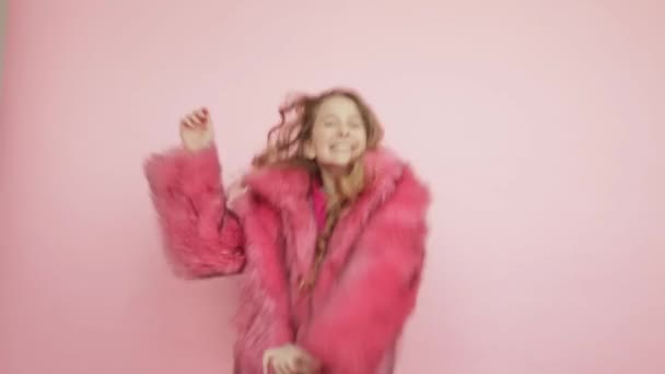 Ένα νεαρό κορίτσι με μακριά μαλλιά χορεύει με ένα ροζ παλτό σε ροζ φόντο.. — Αρχείο Βίντεο