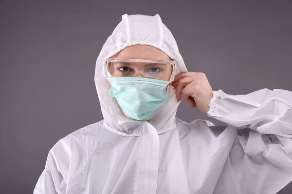 Young woman in protective costume and glasses puts on a protective mask. Protected against coronavirus, flu, ebola, tuberculosis, virus. Personal protective equipment against COVID-19.