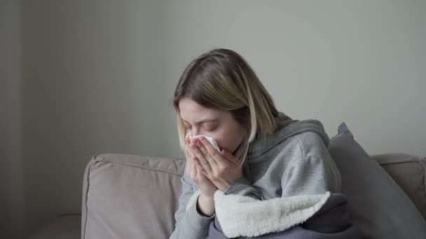 Gros plan. La fille blonde aux cheveux courts s'assoit en pleine croissance, enveloppée dans une couverture, est malade et éternue dans une serviette jetable. Symptôme d'Orvi, coronovirus, grippe, maladie respiratoire aiguë, allergie — Video