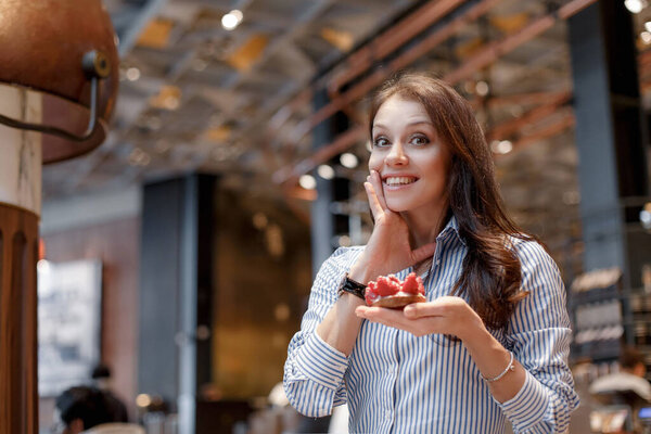 A beautiful girl sits in a cafe and is surprised at a beautiful mouth-watering strawberry dessert.